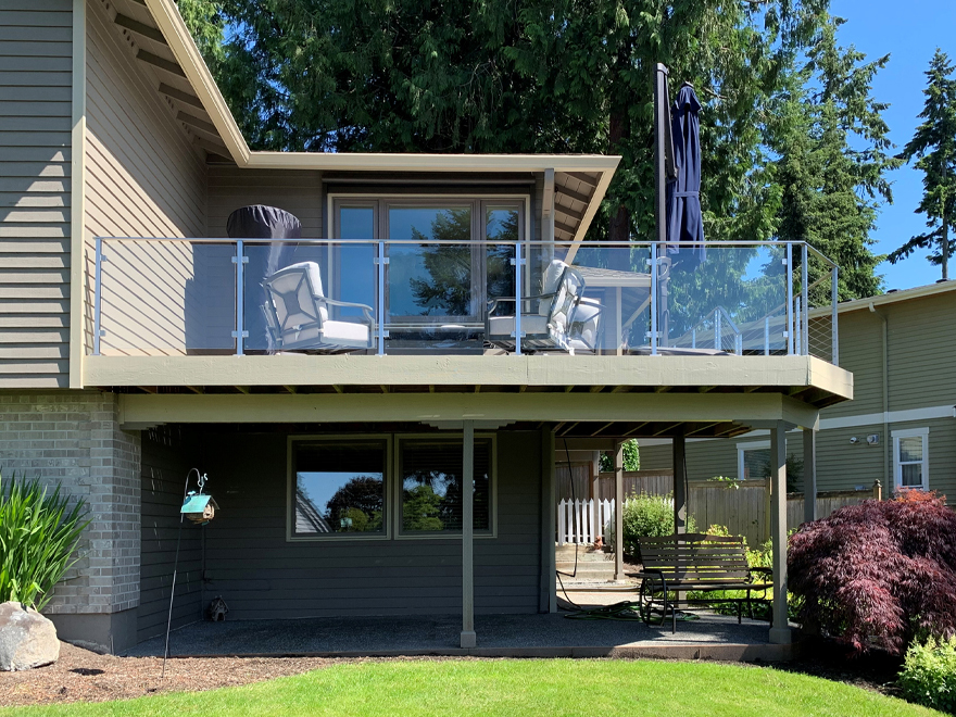 Glass railing design for a balcony and wrap around deck. At the front of the property a glass porch railing overlooks the lush green lawn.